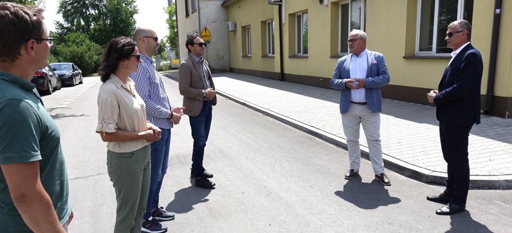 Uczestnicy odbioru (sześć osób) stoją na przebudowanej drodze przy budynku byłego dworca PKP w Drzewicy