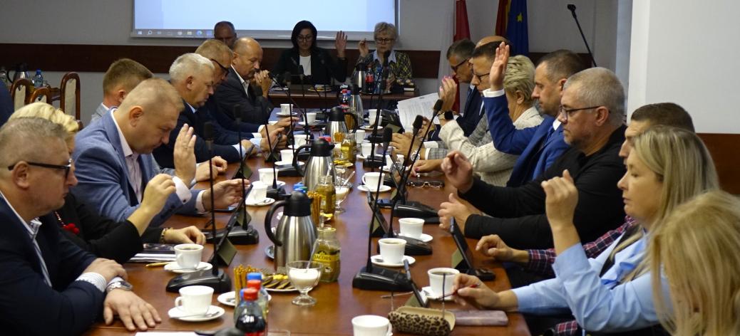 Uczestnicy sesji siedzą przy stołach w sali konferencyjnej Urzędu Miejskiego w Drzewicy. Radni biorą udział w głosowaniu
