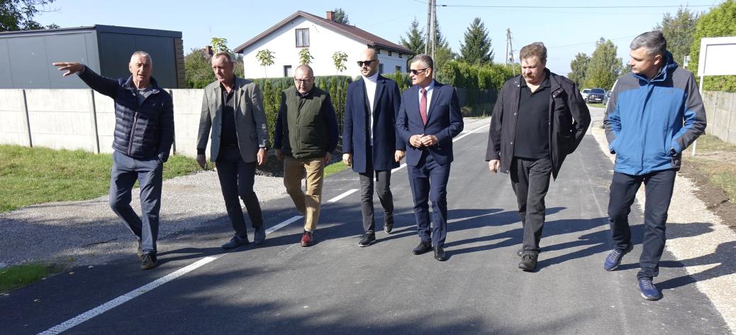 Wyremontowaną drogą w Brzustowcu – Starej Wsi idą uczestnicy odbioru – siedmiu mężczyzn.