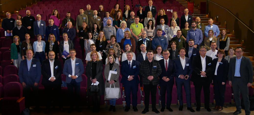 Wspólne zdjęcie uczestników spotkania stojących w rzędach na widowni sali kinowo-widowiskowej RCK