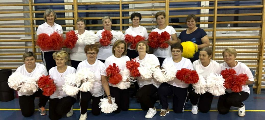 Wspólne zdjęcie seniorek z grupy „Radzice” - czternastu pań trzymających biało-czerwone pompony. Sześć pań stoi, osiem kuca