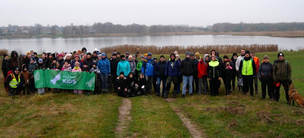 Wspólne zdjęcie kilkudziesięcioosobowej grupy piechurów stojących na trawie na tle Zalewu Drzewickiego