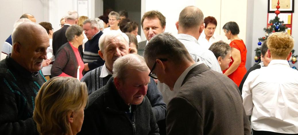 Uczestnicy spotkania - kilkadziesiąt osób – łamią się opłatkiem, składając sobie wzajemnie życzenia