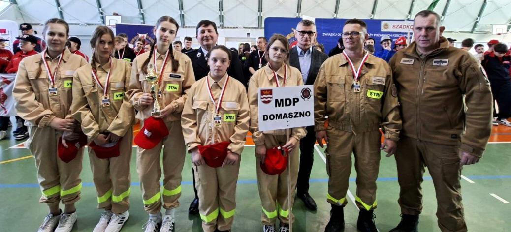 W hali sportowej stoi pięcioosobowa drużyna dziewcząt z OSP Domaszno wraz z opiekunem, Gminnym Komendantem ZOSP w Drzewicy, Burmistrzem Drzewicy i Prezesem Oddziału Powiatowego ZOSP RP w Opocznie.  Dziewczęta mają medale i puchar.