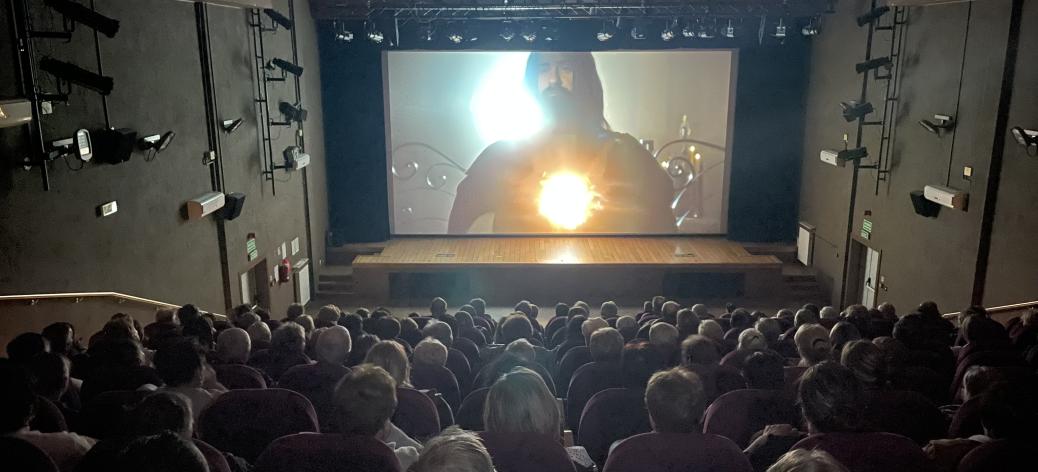 Projekcja filmu w sali widowiskowej drzewickiego RCK_Zdjęcie wykonane z najwyższego rzędu_ widoczna publiczność oraz ekran