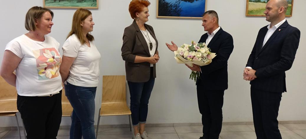 Kameralna uroczystość w sali z obrazami na ścianach. Burmistrz Drzewicy wręcza Dyrektor RCK bukiet kwiatów w obecności Zastępcy Burmistrza i dwóch pracownic RCK.