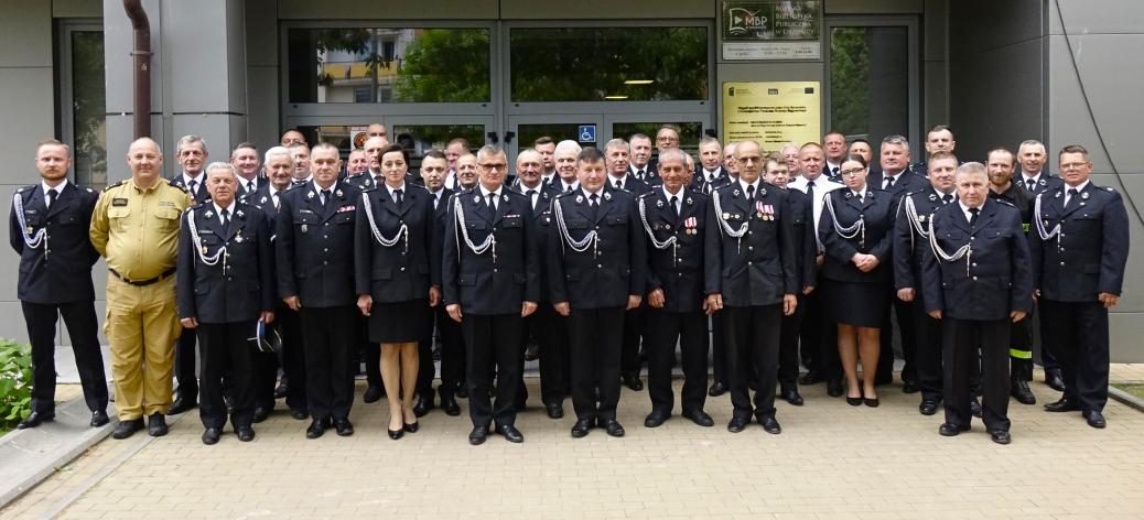 Zdjęcie grupowe kilkudziesięciu strażaków OSP w galowych mundurach i jednego strażaka w piaskowym mundurze służbowym PSP, stojących przed wejściem do budynku Regionalnego Centrum Kultury w Drzewicy