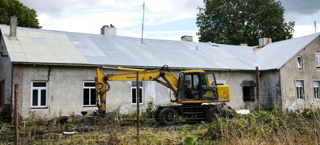  Żółta koparka Komatsu zaparkowana przed starym budynkiem „Ceglanki”.