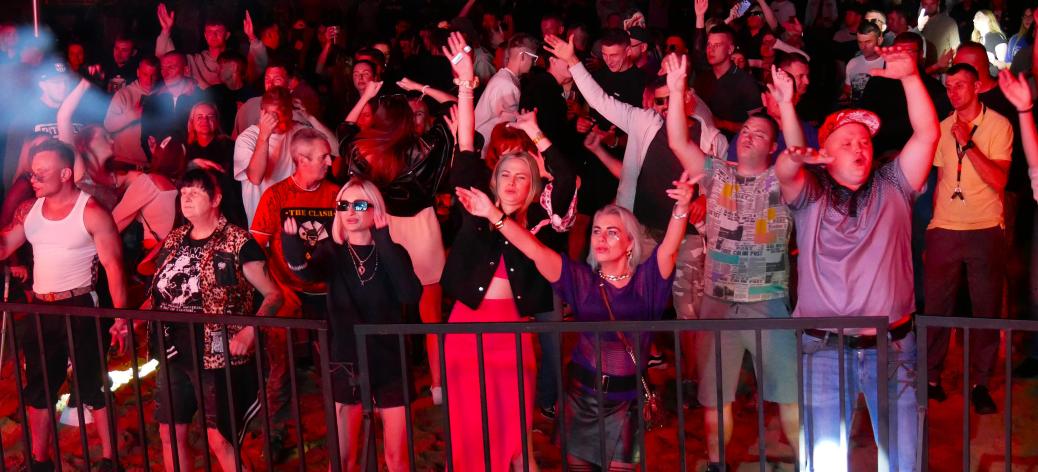 Tłum ludzi bawiący się i tańczący przy barierce pod sceną na plenerowym festiwalu w Drzewicy. Widok nocny.