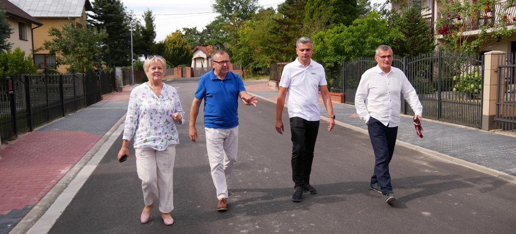 Cztery osoby idą nowo wyasfaltowaną ulicą osiedlową w otoczeniu domów jednorodzinnych na Osiedlu Słonecznym.