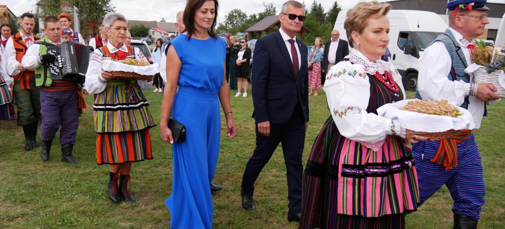  Korowód dożynkowy idący po trawie – na czele osoby w strojach ludowych z chlebami oraz przedstawiciele władz Gminy Drzewica. 