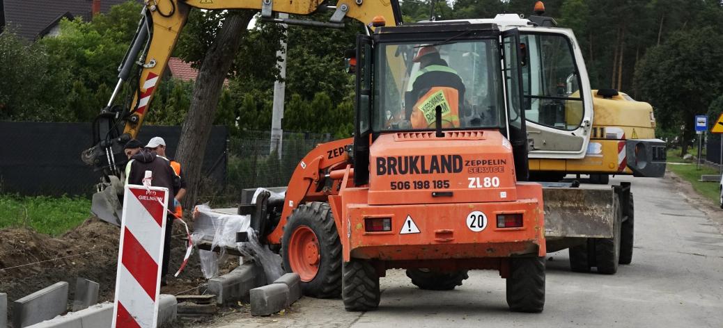 Pomarańczowa ładowarka kołowa z napisem Brukland oraz żółta koparka Liebherr na placu budowy drogi powiatowej Drzewica – Dąbrówka.