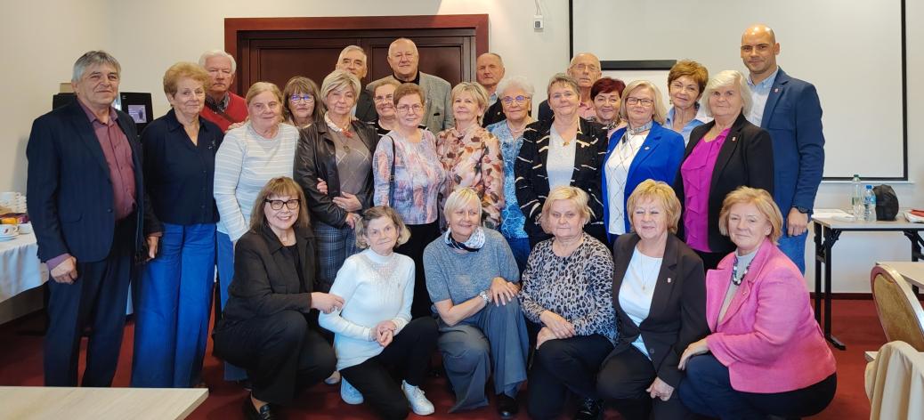 Pamiątkowe zdjęcie grupy uczestników i organizatorów spotkania rad seniorów, ustawionych w kilku rzędach w sali konferencyjnej. 