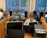 Sześcioro młodzieżowych radnych siedzi przy komputerach w klasopracowni komputerowej. W centralnej części zdjęcia dwóch uczniów