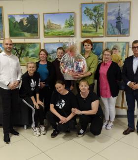 Pamiątkowa wspólna fotografia. Na tle ściany z obrazami, władze samorządowe Gminy Drzewica wraz z dyrekcją oraz pracownikami RCK w Drzewicy