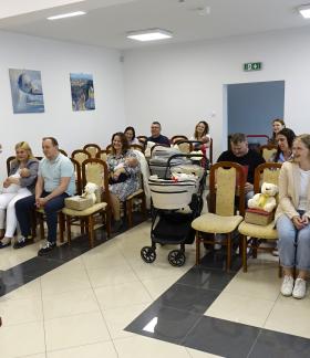 Widok ogólny na salę USC. Rodzice z bobasami siedzą na krzesłach. Przed nimi głos zabiera Burmistrz Drzewicy Janusz Reszelewski
