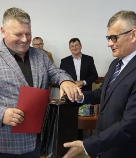 Wojciech Woźniak z uśmiechem na twarzy odbiera od Burmistrza Drzewicy Janusza Reszelewskiego zaświadczenie o wyborze na sołtysa Augustowa i teczkę sołtysa