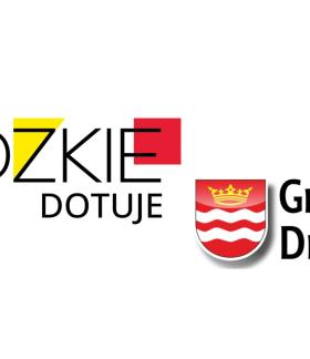 Na białym tle napisy - z lewej ,,Łódzkie dotuje'', z prawej nieco na dole ,,Gmina Drzewica'' wraz z herbem Drzewicy
