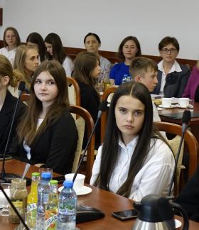 Uczestnicy sesji siedzą przy stołach w sali konferencyjnej Urzędu Miejskiego w Drzewicy. W centrum zdjęcia młodzieżowe radne, z tyłu m.in. nauczycielki.