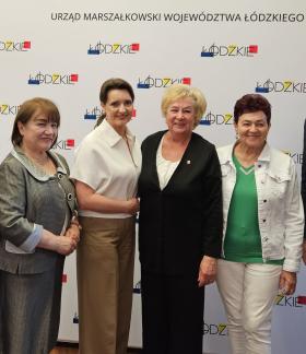 Przed ścianką promocyjną Urzędu Marszałkowskiego Województwa Łódzkiego stoją od lewej: radna senioralna Zdzisława Majchrowska, Przewodnicząca Rady Seniorów Województwa Łódzkiego Krystyna Ozga, Minister ds. Polityki Senioralnej Marzena Okła-Drewnowicz, Przewodnicząca Miejskiej Rady Seniorów w Drzewicy Barbara Oliwa, radna senioralna Jadwiga Szcześniak, Zastępca Burmistrza Drzewicy Dominik Niemirski