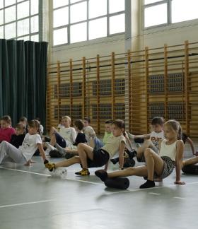Na zdjęciu uczniowie trzecich klas szkół podstawowych z terenu Gminy Drzewica znajdują się w hali sportowej SP w Drzewicy przy ul. Staszica. Wykonują ćwiczenia praktyczne z rollerami. Rolują łydkę. 