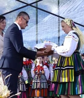 Na scenie Burmistrz Drzewicy Janusz Reszelewski odbiera bochen chleba od dożynkowej starościny Marty Jakubczyk. Obok Burmistrza stoi  Przewodnicząca Rady Miejskiej w Drzewicy Dorota Wiktorowicz.