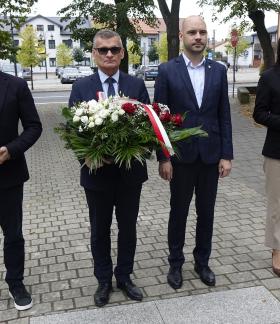 Gminna delegacja w parku na placu Wolności. Od lewej stoją: Sekretarz Miasta Andrzej Krzyżanowski ze zniczem,  Burmistrz Drzewicy Janusz Reszelewski z wiązanką kwiatów, Zastępca Burmistrza Dominik Niemirski, Przewodnicząca Rady Miejskiej w Drzewicy Dorota Wiktorowicz ze zniczem.