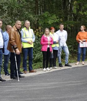 Na wyremontowanej drodze powiatowej stoją uczestnicy odbioru inwestycji – 11 osób. W tle las