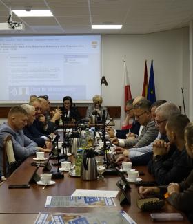 Obrady Nadzwyczajnej Sesji Rady Miejskiej w Drzewicy na sali konferencyjnej Urzędu Miejskiego w Drzewicy. Radni na pierwszym planie zasiadają przy stole. Na drugim planie prezydium rady przy stole.  