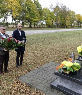 Pomnik nagrobny, po lewej stoją Burmistrz Drzewicy Janusz Reszelewski trzymający wieniec i Zastępca Burmistrza Drzewicy Dominik Niemirski trzymający znicz. W tle pas drogi wojewódzkiej. 