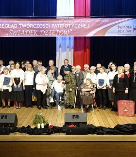  Wspólne zdjęcie wykonawców i organizatorów przeglądu po uroczystej dekoracji. Na scenie stoi kilkadziesiąt osób, nad którymi wisi baner z nazwą imprezy