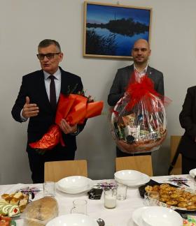 Podczas oficjalnej części uroczystości przemawia trzymający bukiet kwiatów Burmistrz Drzewicy Janusz Reszelewski. Po lewej stronie Burmistrza stoi Przewodnicząca Koła Emerytów i Rencistów Jadwiga Gapys, po prawej stoją Zastępca Burmistrza Dominik Niemirski z koszem słodkości i Prezes CAL w Drzewicy Edyta Bartos, a także siedzi jeden z emerytów.  