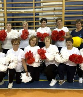 Wspólne zdjęcie seniorek z grupy „Radzice” - czternastu pań trzymających biało-czerwone pompony. Sześć pań stoi, osiem kuca