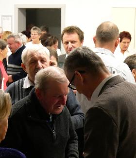 Uczestnicy spotkania - kilkadziesiąt osób – łamią się opłatkiem, składając sobie wzajemnie życzenia