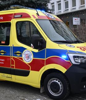Ambulans w kolorach żółtym, niebieskim i czerwonym stroi na parkingu przed budynkiem szpitala w Opocznie