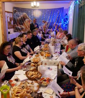 Przy zastawionym stole w siedzibie KGW w Radzicach Małych kolędują Burmistrz Janusz Reszelewski wraz z mieszkańcami sołectwa. 