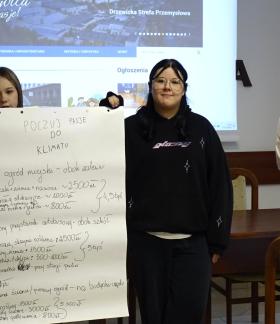 W sali konferencyjnej UM na tle ekranu stoi czworo uczniów. Jedna z dziewcząt trzyma zapisany duży arkusz papieru