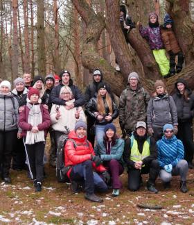 Wspólne zdjęcie kilkudziesięcioosobowej grupy piechurów w lesie na tle drzew