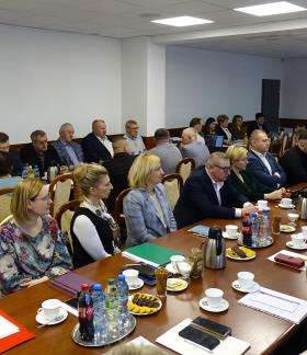 Kilkadziesiąt osób uczestniczących w sesji siedzi przy stołach w sali konferencyjnej Urzędu Miejskiego w Drzewicy. Widok ogólny z góry.