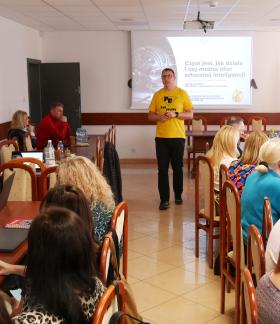 Przy stołach w sali konferencyjnej UM w Drzewicy siedzą nauczyciele, niektórzy z laptopami. W środku na tle ekranu stoi prowadzący szkolenie, ubrany w żółty t-shirt.