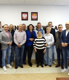 Grupa kilkunastu osób - społeczników i samorządowców - stoi w sali konferencyjnej UM w Drzewicy na tle ściany z godłem Polski i herbem Drzewicy