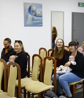 W sali USC Burmistrz Janusz Reszelewski mówi do siedzących na krzesłach rodziców z maluchami