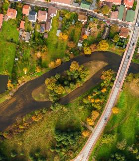 Widok z lotu ptaka na jesienny krajobraz w Drzewicy, przedstawiający ruiny gotycko-renesansowego zamku, rzekę Drzewiczkę z jazem, które otoczone są kolorowymi drzewami i zabudową miejską.
