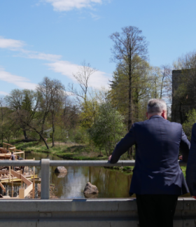 Na moście w Drzewicy stoją Marszałek Województwa Łódzkiego, Zastępca Dyrektora RCPS w Łodzi oraz Burmistrz Drzewicy, w tle budowa bulwaru, rzeka Drzewiczka oraz biskupi zamek w Drzewicy