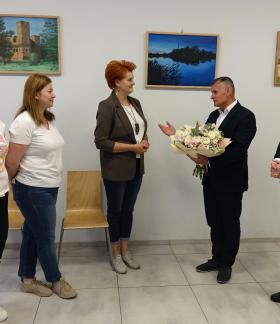Kameralna uroczystość w sali z obrazami na ścianach. Burmistrz Drzewicy wręcza Dyrektor RCK bukiet kwiatów w obecności Zastępcy Burmistrza i dwóch pracownic RCK.