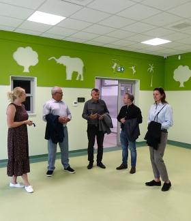 Grupa pięciu osób rozmawia w dużej, jasnej sali z zielonymi dekoracjami ściennymi przedstawiającymi zwierzęta.