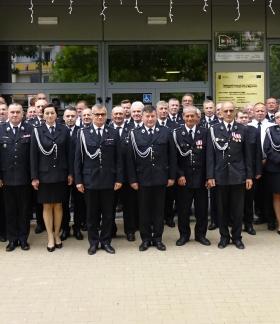 Zdjęcie grupowe kilkudziesięciu strażaków OSP w galowych mundurach i jednego strażaka w piaskowym mundurze służbowym PSP, stojących przed wejściem do budynku Regionalnego Centrum Kultury w Drzewicy