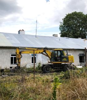  Żółta koparka Komatsu zaparkowana przed starym budynkiem „Ceglanki”.