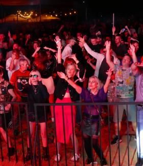 Tłum ludzi bawiący się i tańczący przy barierce pod sceną na plenerowym festiwalu w Drzewicy. Widok nocny.