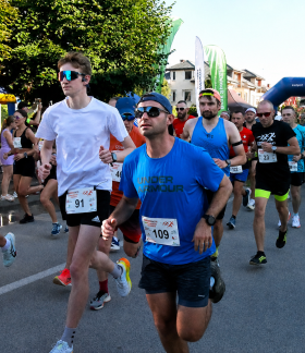 Grupa biegaczy w trakcie wyścigu ulicznego Drzewica Summer Run. Na pierwszym planie mężczyzna w niebieskiej koszulce z numerem 109 i okularach przeciwsłonecznych, obok biegacz w białej koszulce.